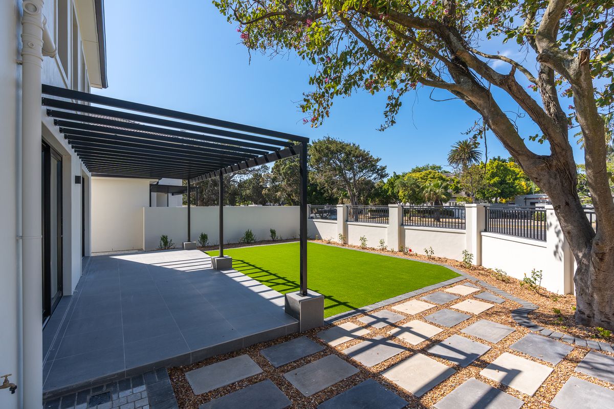 A well-maintained rear garden featuring a modern tiled patio with a black pergola, artificial lawn, and secure perimeter walling.