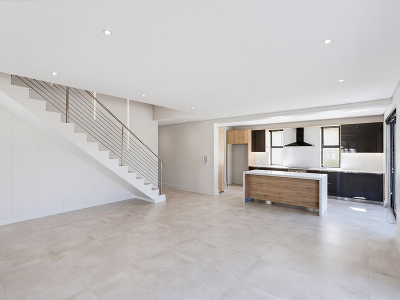 Spacious open-plan living area featuring a modern kitchen with island, sleek cabinetry, and a contemporary staircase with stainless steel balustrades.