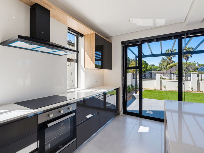 Modern kitchen featuring sleek gloss cabinetry, stone countertops, built-in appliances, and direct access to the outdoor patio and garden area.