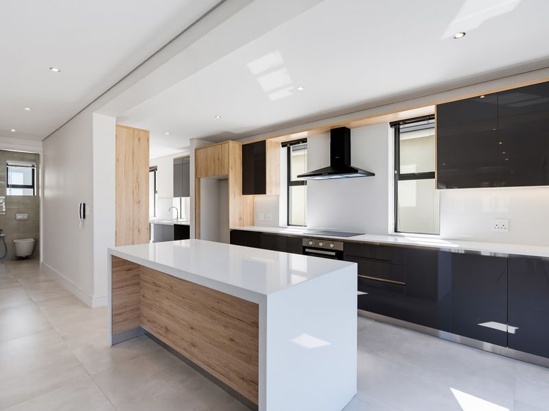 Modern kitchen featuring a central island, sleek dark cabinetry with wood accents, quartz countertops, and integrated appliances, finished with high-quality tiled flooring.