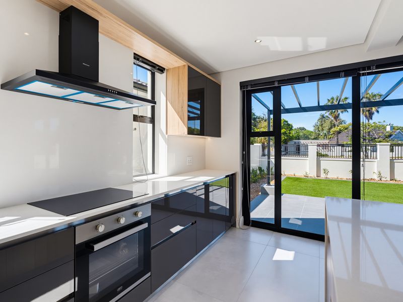 Modern kitchen featuring sleek gloss cabinetry, quartz countertops, built-in oven, and hob, with direct access to the rear patio and garden.