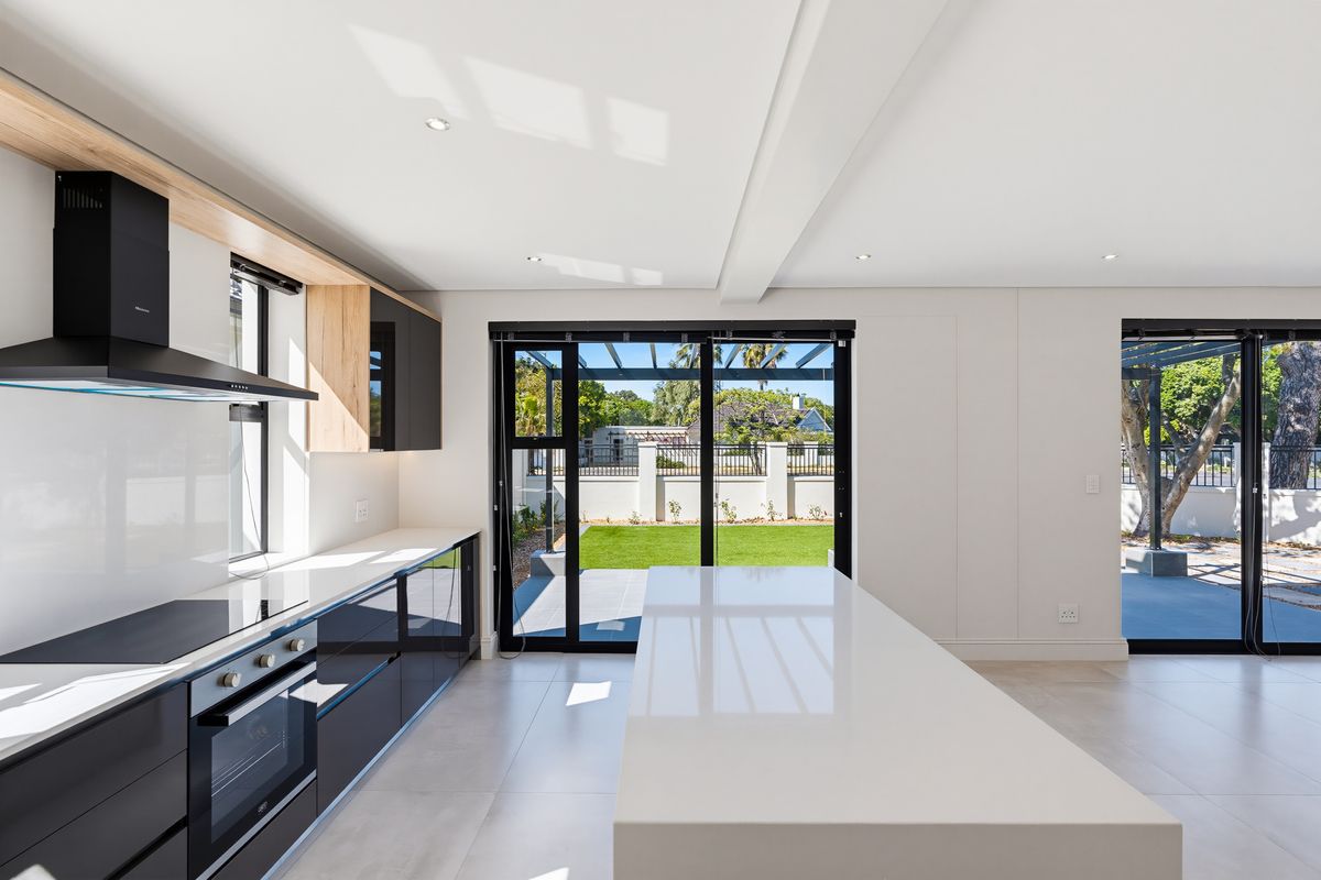 Modern kitchen featuring sleek black cabinetry, a large central island with stone countertops, integrated appliances, and direct access to the rear garden.