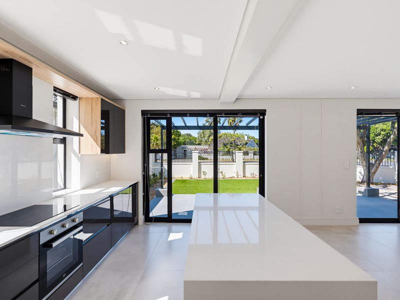 Modern kitchen featuring sleek black cabinetry, a large central island with stone countertops, integrated appliances, and direct access to the rear garden.