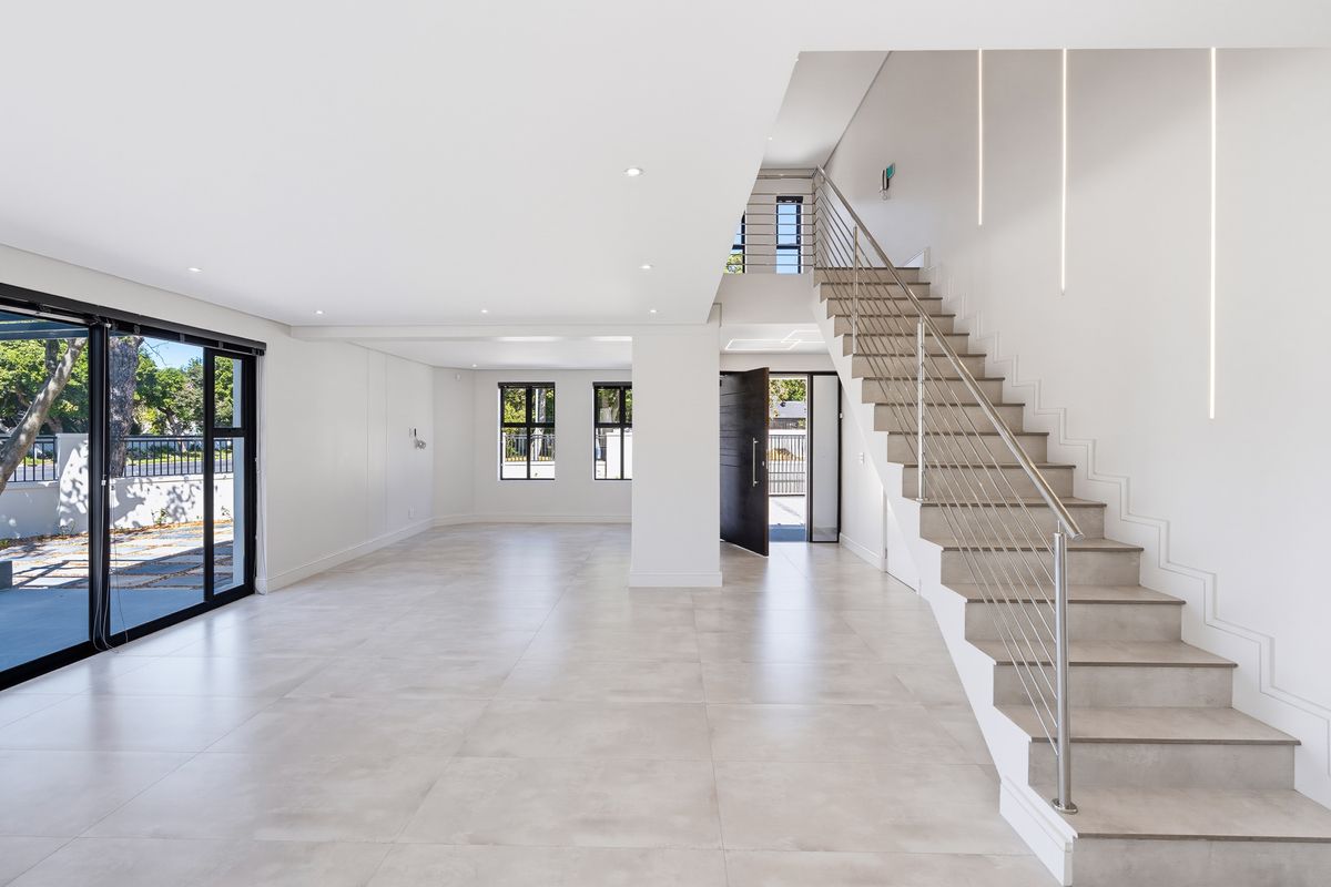 Spacious, modern open-plan living area featuring large format floor tiles, a contemporary staircase with stainless steel balustrade, and abundant natural light.