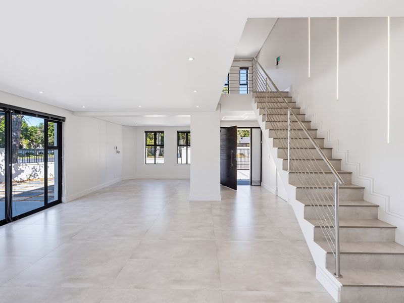 Spacious, modern open-plan living area featuring large format floor tiles, a contemporary staircase with stainless steel balustrade, and abundant natural light.
