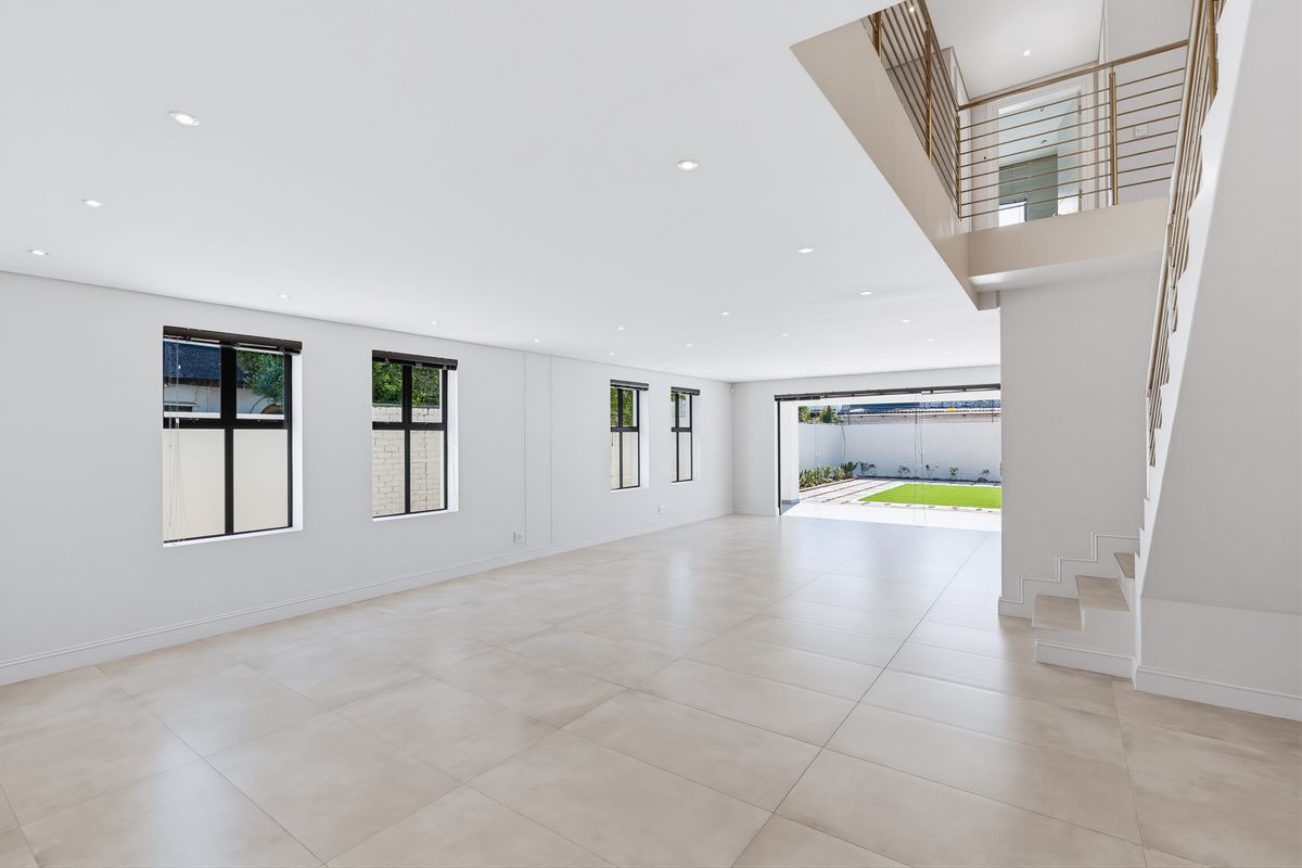 Spacious, light-filled open-plan living area featuring large format floor tiles, recessed lighting, and a modern staircase leading to an upper level.
