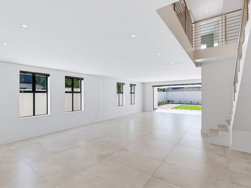 Spacious, light-filled open-plan living area featuring large format floor tiles, recessed lighting, and a modern staircase leading to an upper level.