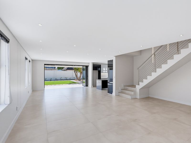 Spacious open-plan living area featuring modern tiled floors, recessed lighting, a sleek staircase with stainless steel balustrade, and bi-fold doors opening to the garden.