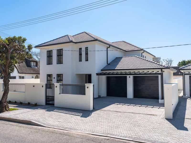 Modern double-story house featuring a clean white facade, double garage, paved driveway, and secure perimeter walling with metal gate.