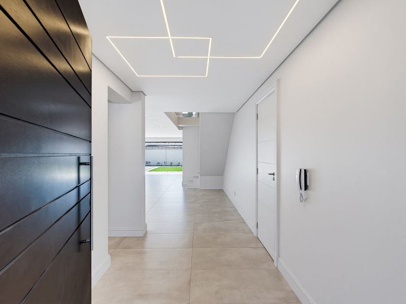 Modern, minimalist entrance hall featuring sleek tiled flooring, recessed geometric ceiling lighting, and a secure intercom system, leading into an open-plan living space.