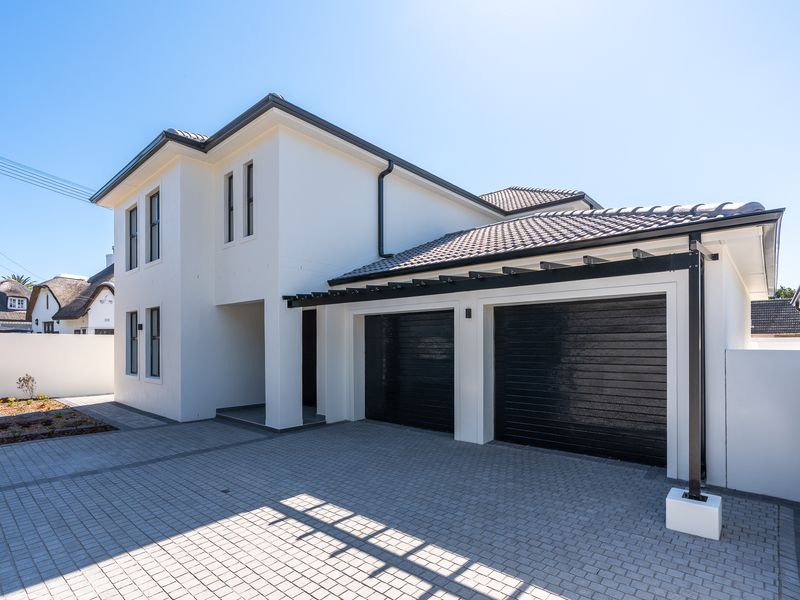 Modern double-storey home exterior featuring a double garage with black sectional doors, a paved driveway, and a contemporary pergola structure.