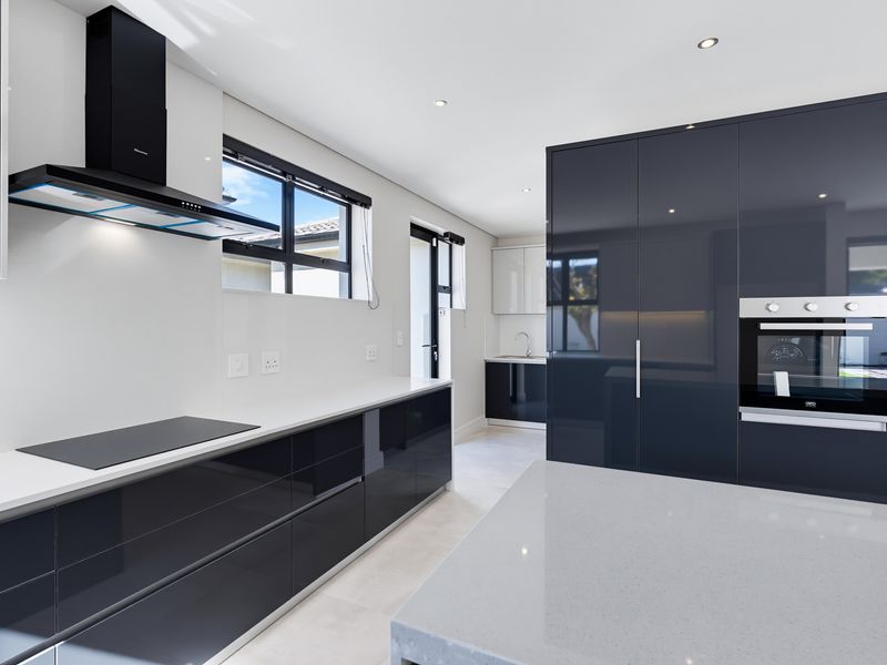 Modern kitchen featuring high-gloss cabinetry, quartz countertops, integrated oven, induction cooktop, and a sleek extractor fan, with a separate scullery area visible.