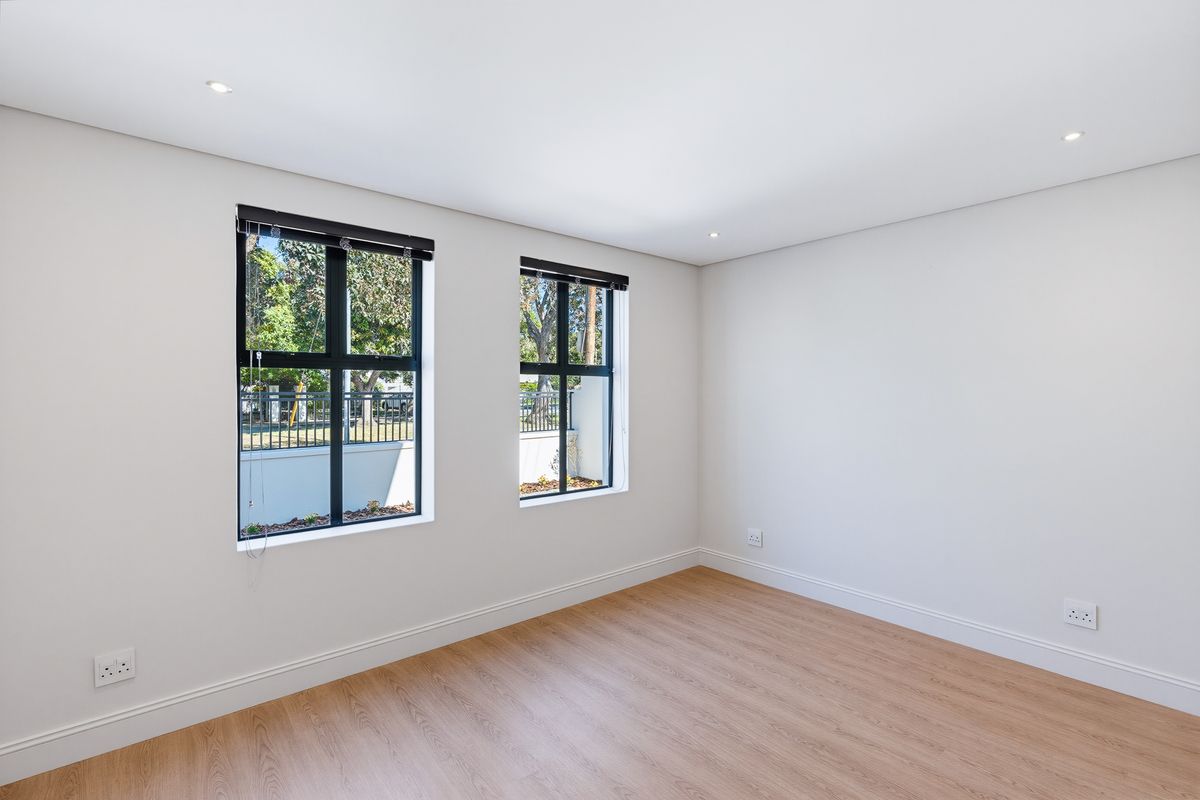 A bright, empty bedroom featuring modern laminate flooring, recessed downlights, and black-framed windows with venetian blinds.