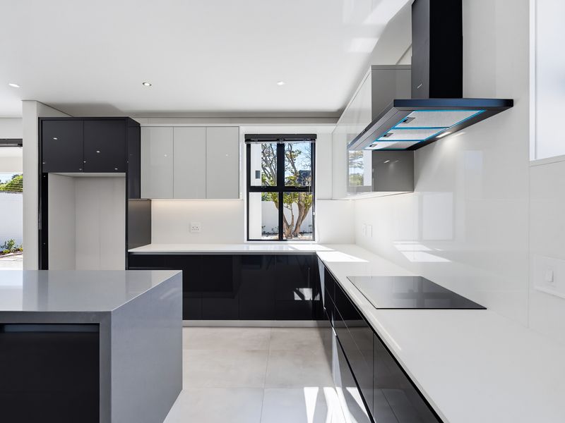 Modern, high-end kitchen featuring sleek two-tone cabinetry, a central island, quartz countertops, and integrated induction hob with extractor fan.