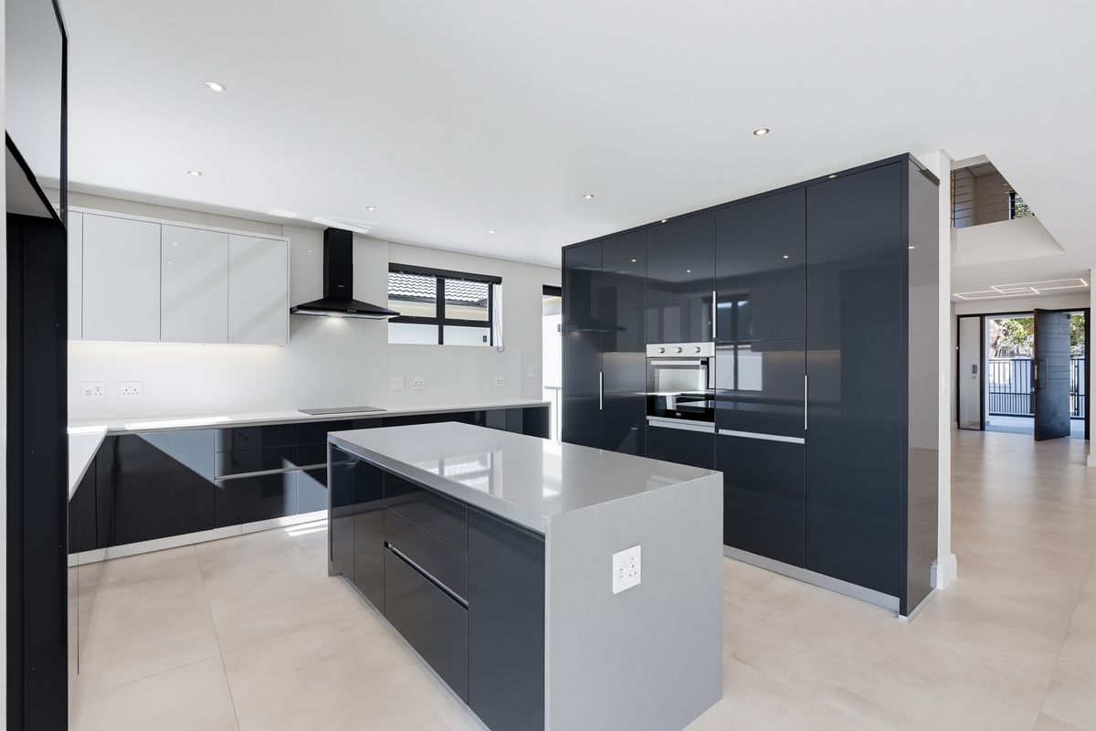 Modern kitchen featuring high-gloss cabinetry, a central island with quartz countertops, built-in oven, and sleek extractor fan in an open-plan layout.