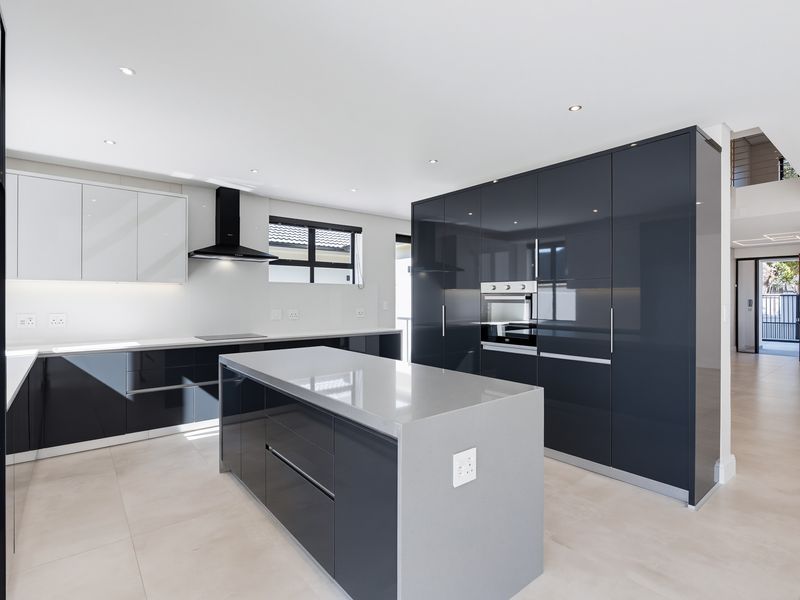Modern kitchen featuring high-gloss cabinetry, a central island with quartz countertops, built-in oven, and sleek extractor fan in an open-plan layout.