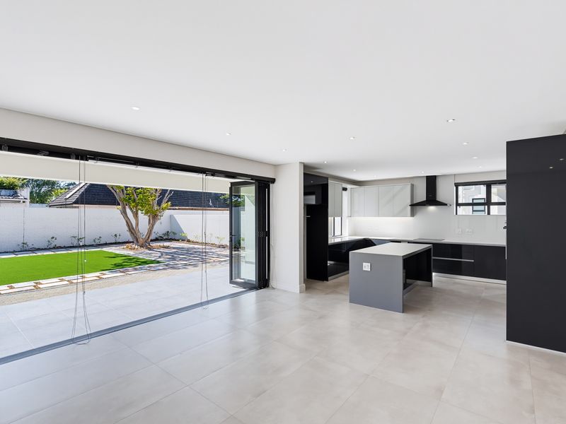 Modern open-plan kitchen and living area featuring sleek cabinetry, a central island, and large stacking doors opening onto a paved patio and garden.