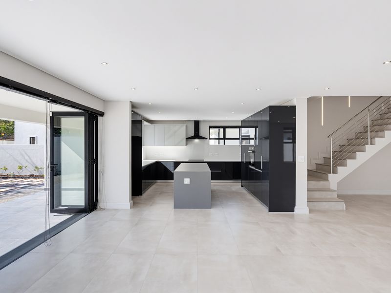 Modern open-plan kitchen featuring sleek cabinetry, a central island, and seamless flow to an outdoor patio area via large stacking doors.