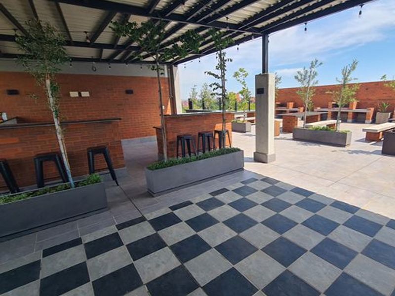 Spacious outdoor rooftop patio featuring a covered area with a built-in brick bar, integrated planters, and checkered stone flooring.