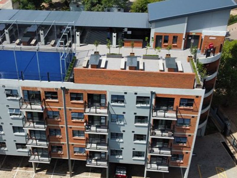 Aerial view of a modern apartment complex featuring a rooftop terrace with a swimming pool, private balconies, and ground-level parking facilities.