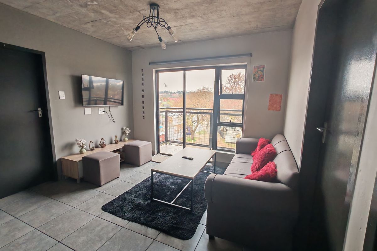 A contemporary living room featuring an exposed concrete ceiling, tiled floors, and a sliding door leading to a balcony with an urban view.