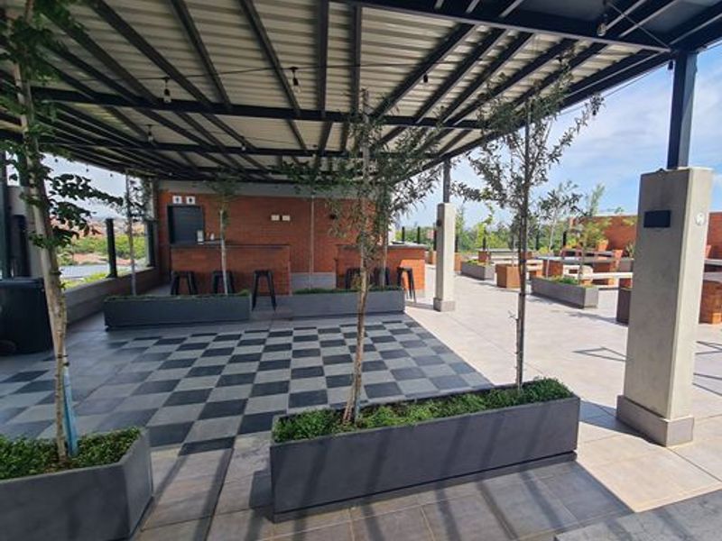 A spacious covered rooftop patio featuring a built-in brick bar, checkerboard tiled flooring, and integrated planters, ideal for outdoor entertaining.