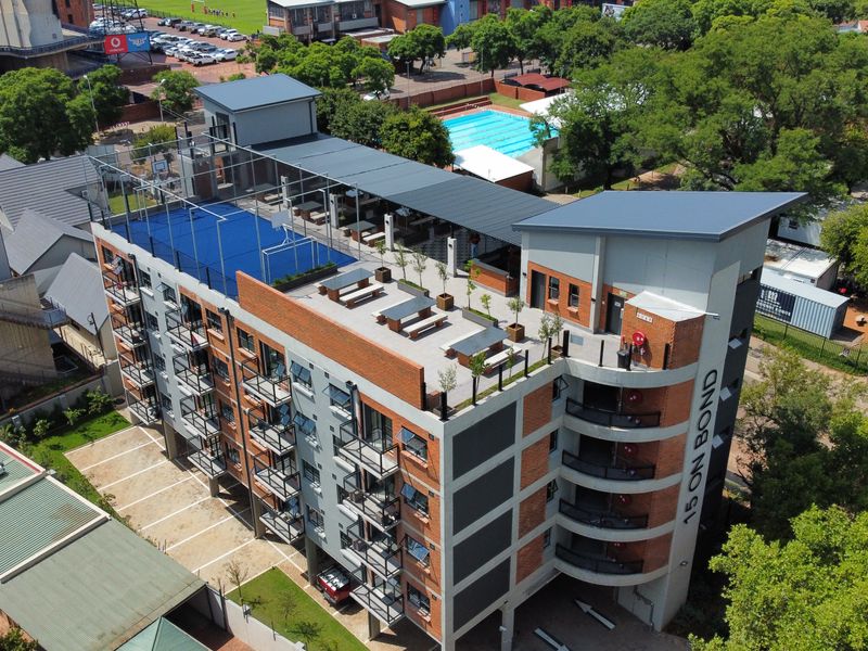 Aerial view of a modern apartment building featuring a rooftop sports court, communal terrace, and private balconies with brick and concrete architectural detailing.