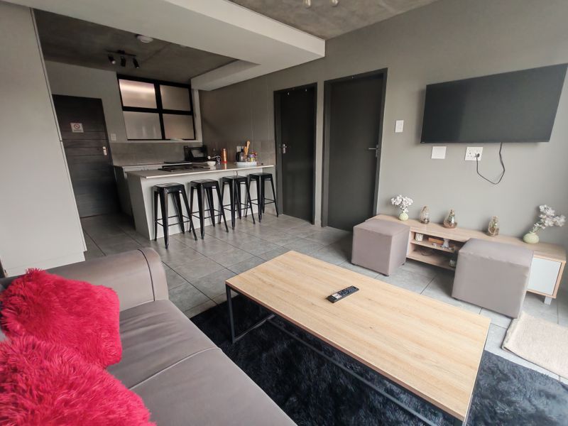 Modern open-plan living area featuring a kitchen island, tiled flooring, and an exposed concrete ceiling, creating a contemporary and functional apartment space.