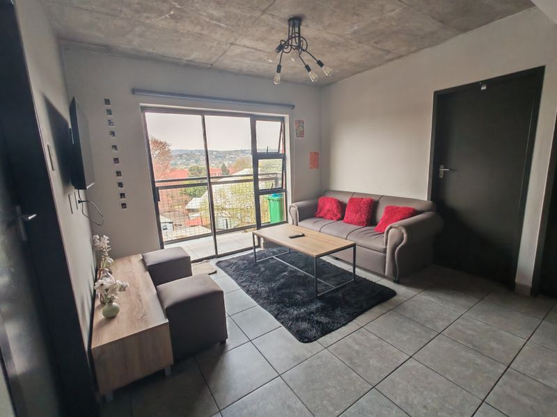 A contemporary living room featuring an exposed concrete ceiling, tiled floors, and a large sliding door providing access to a balcony with neighborhood views.