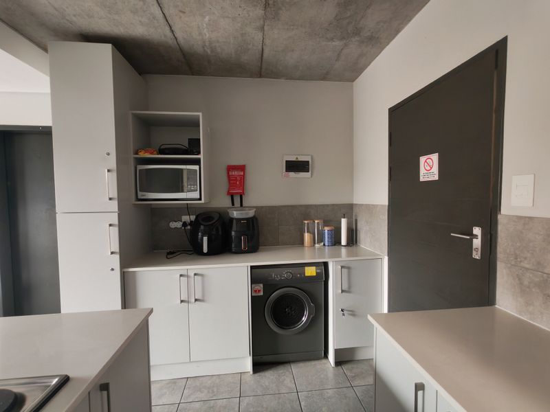 Modern kitchen featuring sleek white cabinetry, stone countertops, tiled backsplash, and an exposed concrete ceiling, with an integrated washing machine.