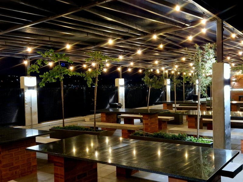 A well-maintained covered outdoor patio area featuring built-in stone tables with brick bases, integrated lighting, and planter boxes, ideal for communal entertainment.