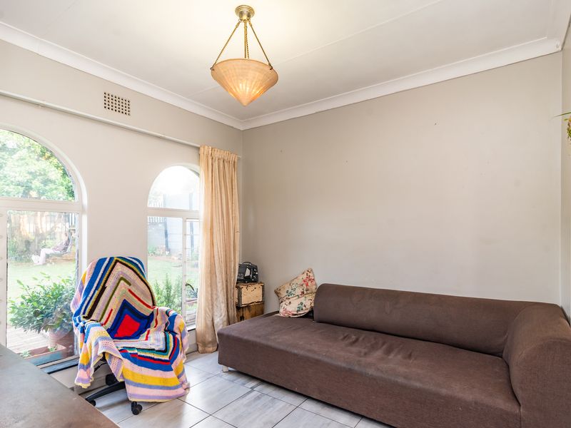 A bright living room featuring arched windows, tiled flooring, and decorative cove cornicing, offering a comfortable space with natural light.