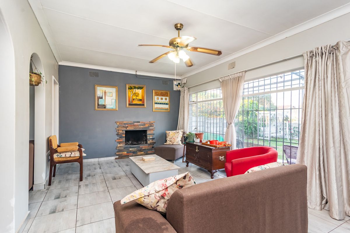 A living room featuring a stone-clad fireplace, tiled flooring, and large windows with security bars, offering a bright and functional living space.