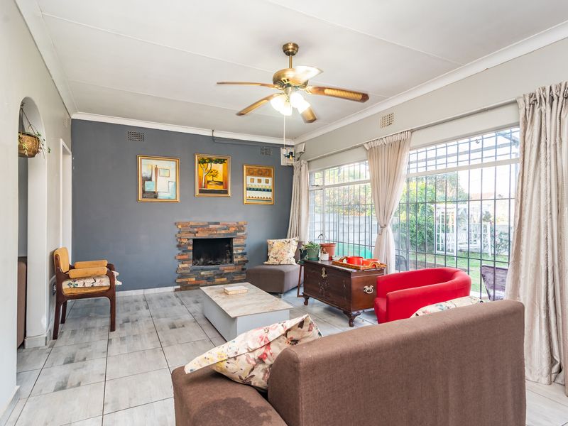 A living room featuring a stone-clad fireplace, tiled flooring, and large windows with security bars, offering a bright and functional living space.