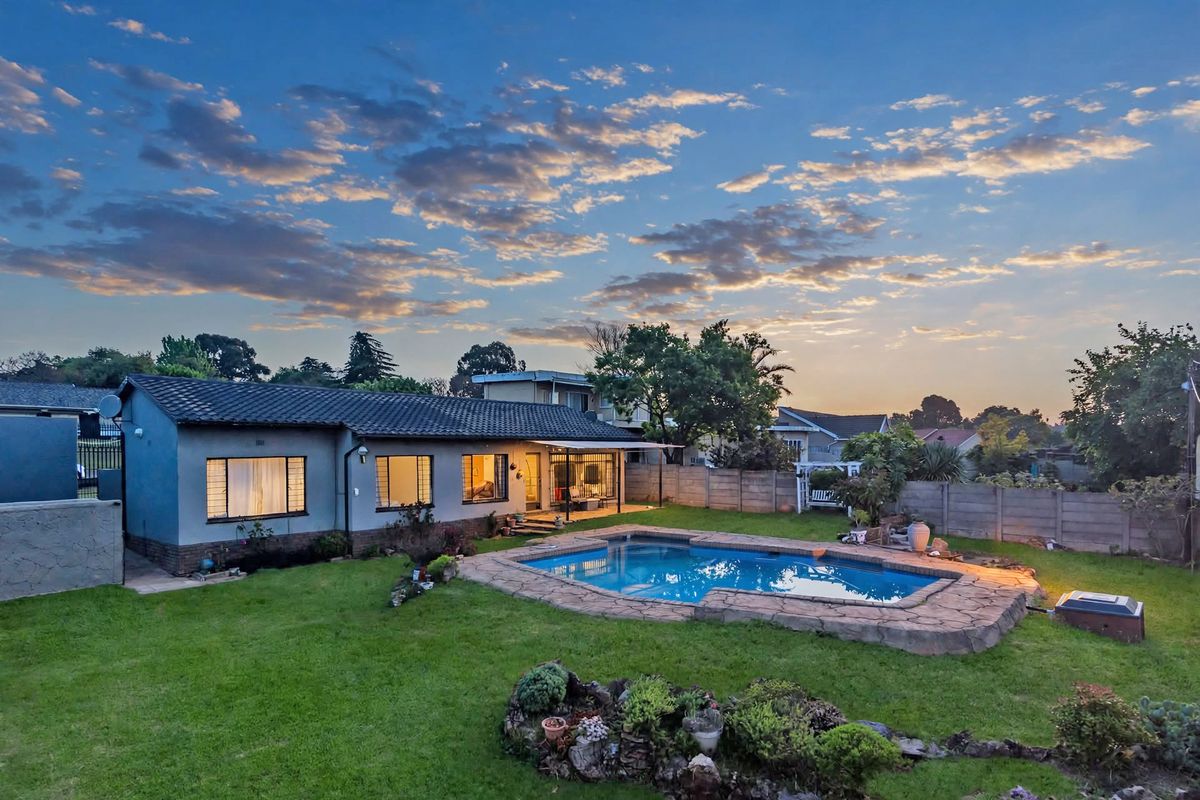 Rear view of the property featuring a swimming pool with stone coping, a well-maintained lawn, and a covered patio area.
