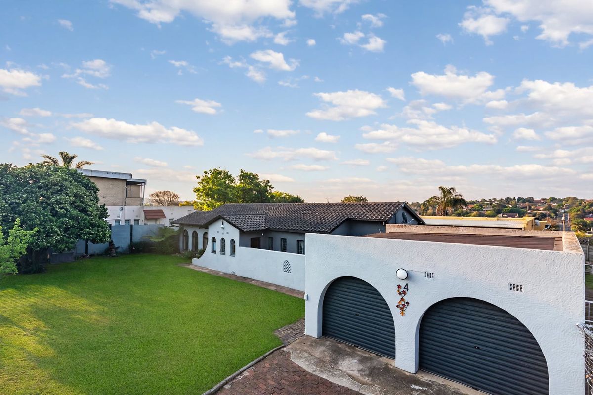 An aerial view of the property showing the main house, a double garage with arched openings, and a well-maintained lawn area.