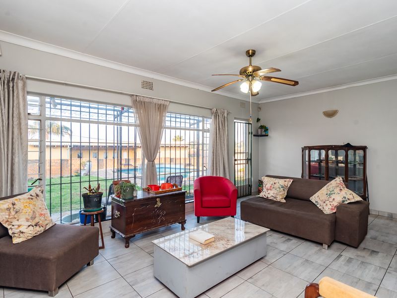 Spacious living room featuring tiled flooring, a ceiling fan, and large sliding glass doors with security bars providing access to the outdoor pool area.
