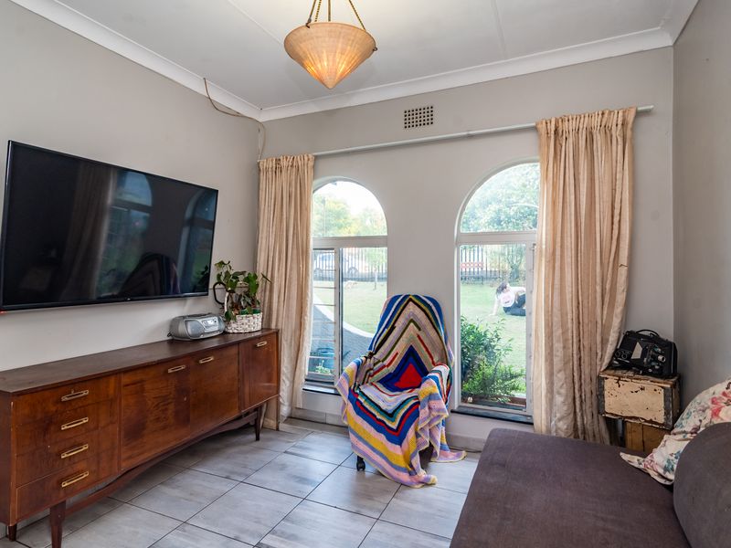A living room featuring arched windows, tiled flooring, and a pendant light fixture, offering a view of the garden.