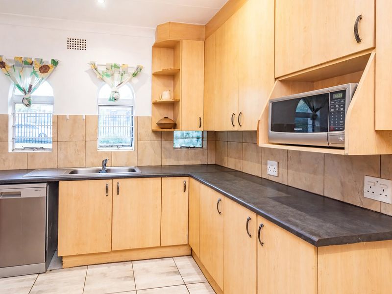 Functional kitchen featuring light wood cabinetry, dark laminate countertops, tiled backsplash, and built-in microwave, with natural light from arched windows.