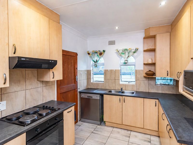 A functional kitchen featuring light wood cabinetry, dark laminate countertops, tiled splashbacks, and integrated appliances including an oven, hob, and extractor fan.