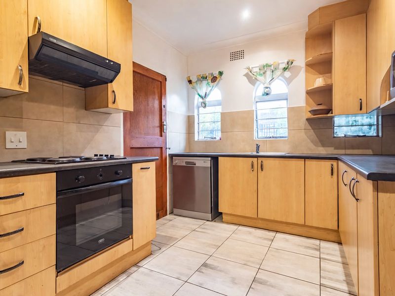 A functional kitchen featuring light wood cabinetry, dark countertops, built-in appliances, and tiled flooring with arched windows providing natural light.