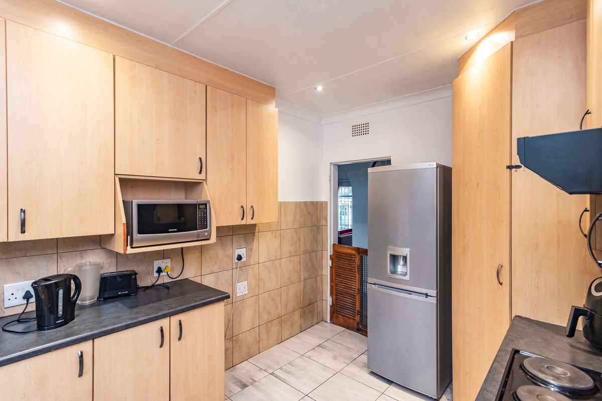 A functional kitchen featuring light wood-finish cabinetry, dark laminate countertops, tiled splashbacks, and tiled flooring with integrated appliances.