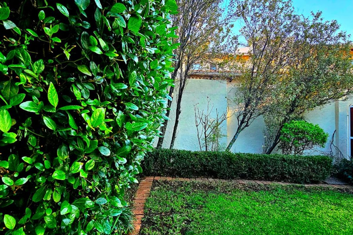 A view of the townhouse rear exterior featuring a well-maintained garden, manicured hedges, and a stucco building facade.