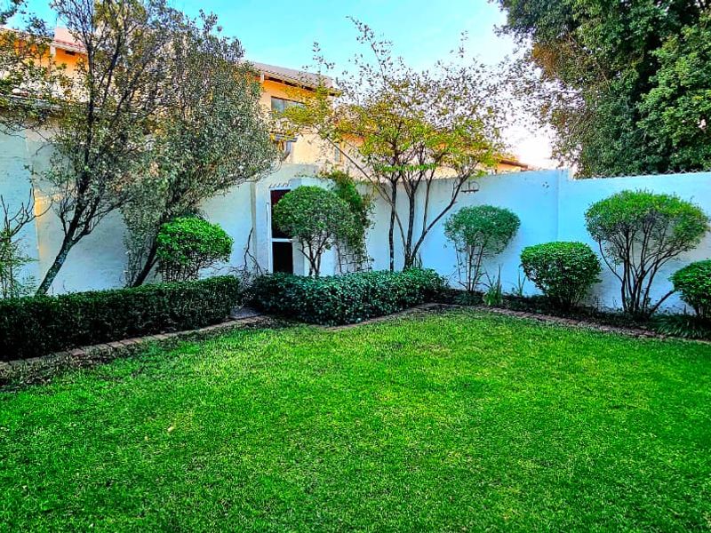 A private rear garden featuring a well-maintained lawn, established shrubs, and a perimeter wall.