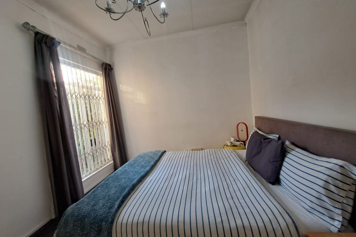 A functional bedroom featuring a security gate on the window, cove cornicing, and a central chandelier light fixture.