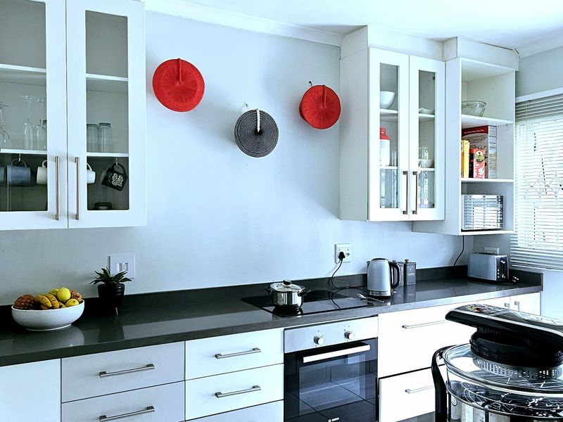Modern kitchen featuring white cabinetry, dark stone countertops, built-in oven, electric hob, and light-toned tiled flooring.