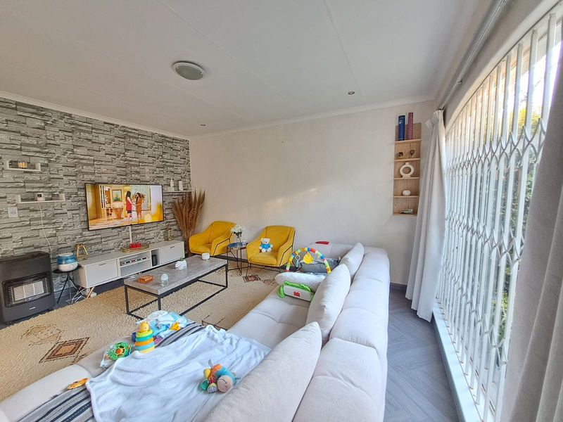 A comfortable living room featuring a textured stone-cladding accent wall, recessed lighting, and large windows secured with a metal security gate.