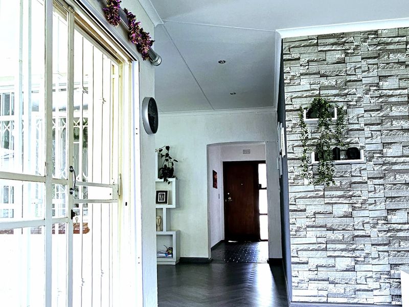 A bright living area featuring modern herringbone flooring, a textured stone veneer feature wall, and direct access to the exterior through a sliding security door.