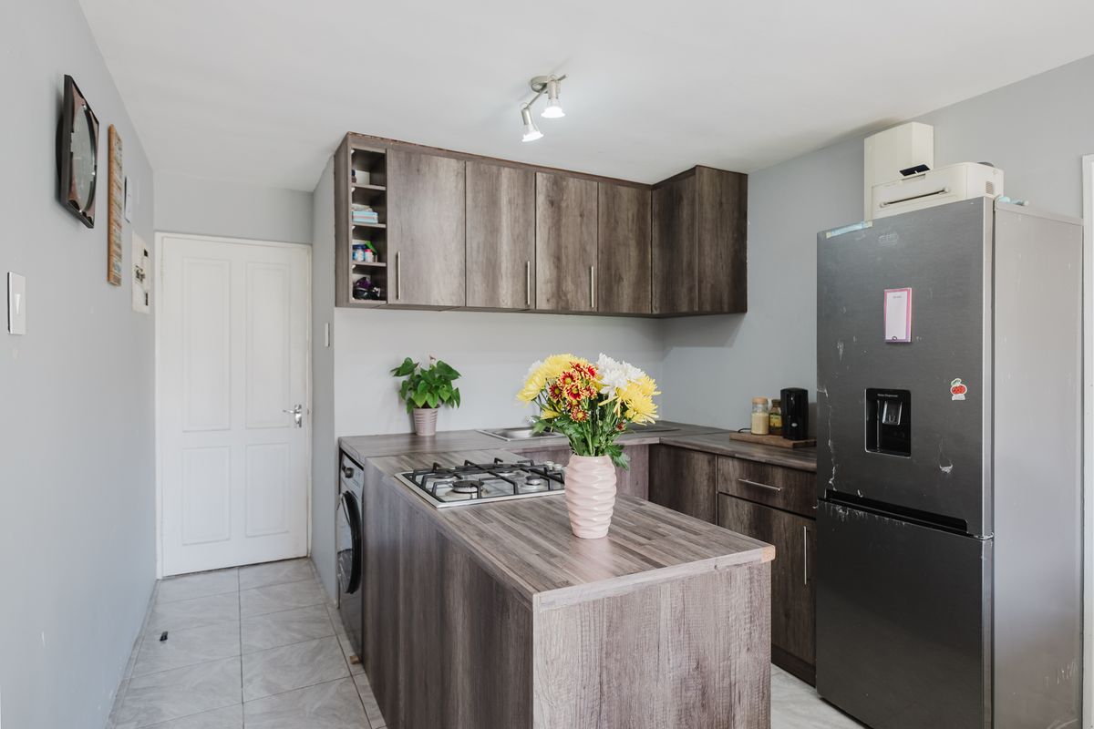 Compact kitchen featuring modern wood-look laminate cabinetry, gas hob, and tiled flooring, offering a functional and efficient workspace.