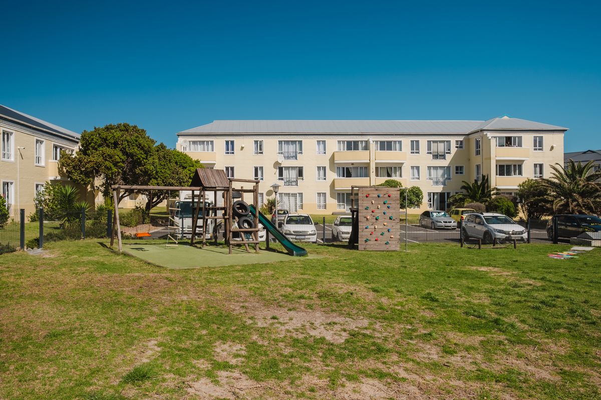View of the communal garden area featuring a playground, lawn, and adjacent parking facilities for the townhouse complex.